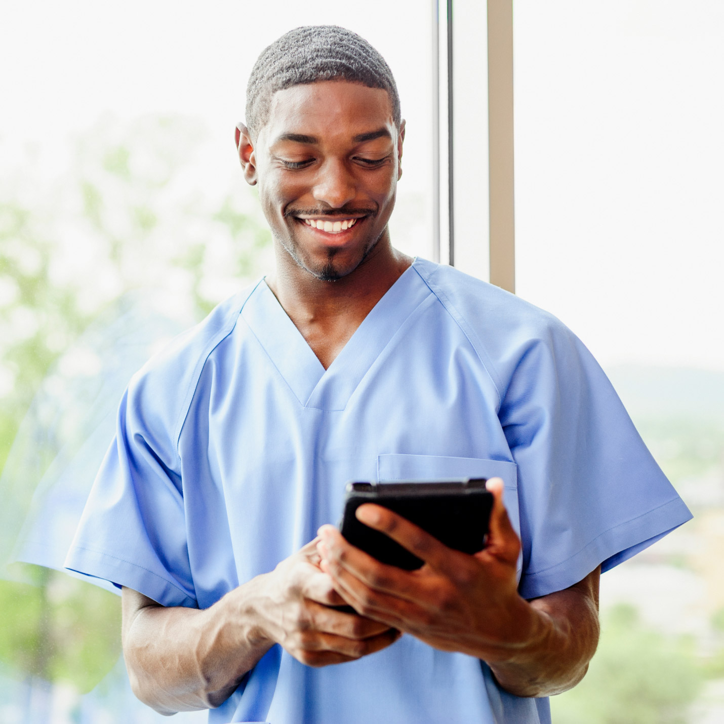 A nurse smiling while reviewing patient info on a tablet during an in-home visit.