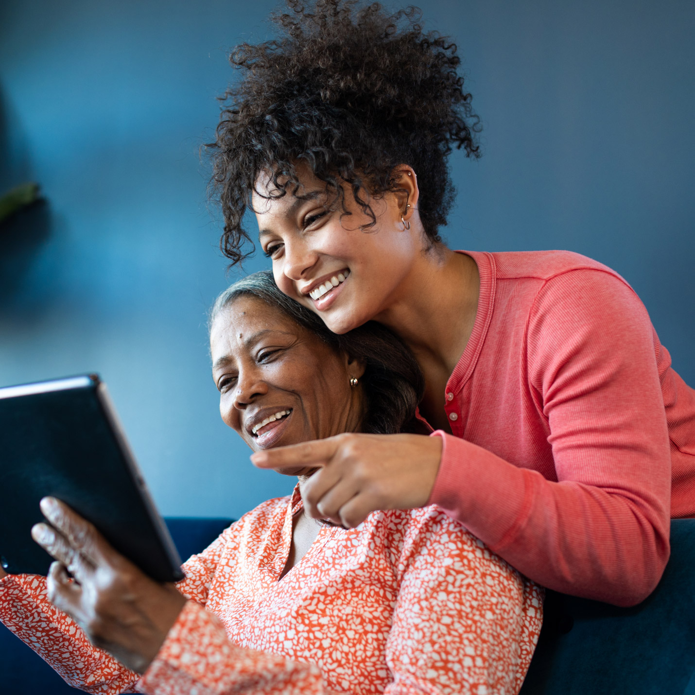 Smiling adult woman behind her mother pointing at an iPad screen her mother is holding